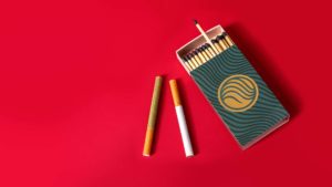 2 different colored cigarettes in Botani Hemp Wrapper next to a Botani Match Box over a red background