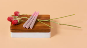 3 Pink Botani Pre-Rolls sitting on a wood case and 3 magenta flowers